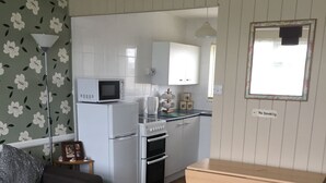 A compact living space with a kitchenette, a sofa, a small table, and a floral-patterned wall. - 2 bed dog Friendly Chalet on Sunbeach Scratby (Great Yarmouth)