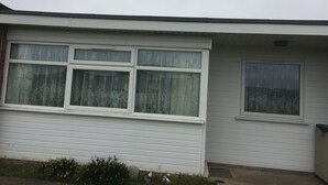 A single-story house with a front porch, a large window with a curtain, and a smaller window to the right. - 2 bed dog Friendly Chalet on Sunbeach Scratby (Great Yarmouth)