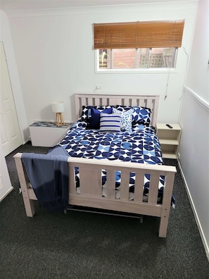 A bedroom with a bed, a nightstand, a lamp, and a window with blinds.