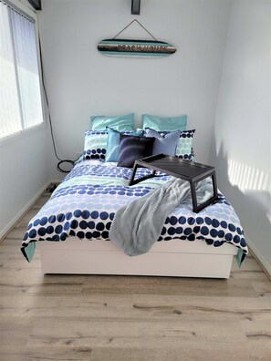A bedroom with a bed, pillows, a bedside table, and a wall-mounted sign. - Beachside Escape, WiFi & Pet-Friendly | Riptide (Lilli Pilli)