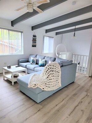 Een moderne woonkamer met een grijze bank, een witte salontafel en een witte geweven stoel.