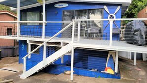 A blue building with a sign reading "Riplide," featuring a covered outdoor area with a chair and a covered grill. - Beachside Escape, WiFi & Pet-Friendly | Riptide (Lilli Pilli)
