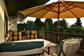 Eine Terrasse im Freien mit Tisch, Stühlen und einem großen Sonnenschirm, an einer Steinmauer entlang.