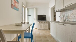 Una cucina compatta con mobili bianchi, un tavolo da pranzo con sedie blu, una TV a parete e un pannello di divisa con motivo decorativo.