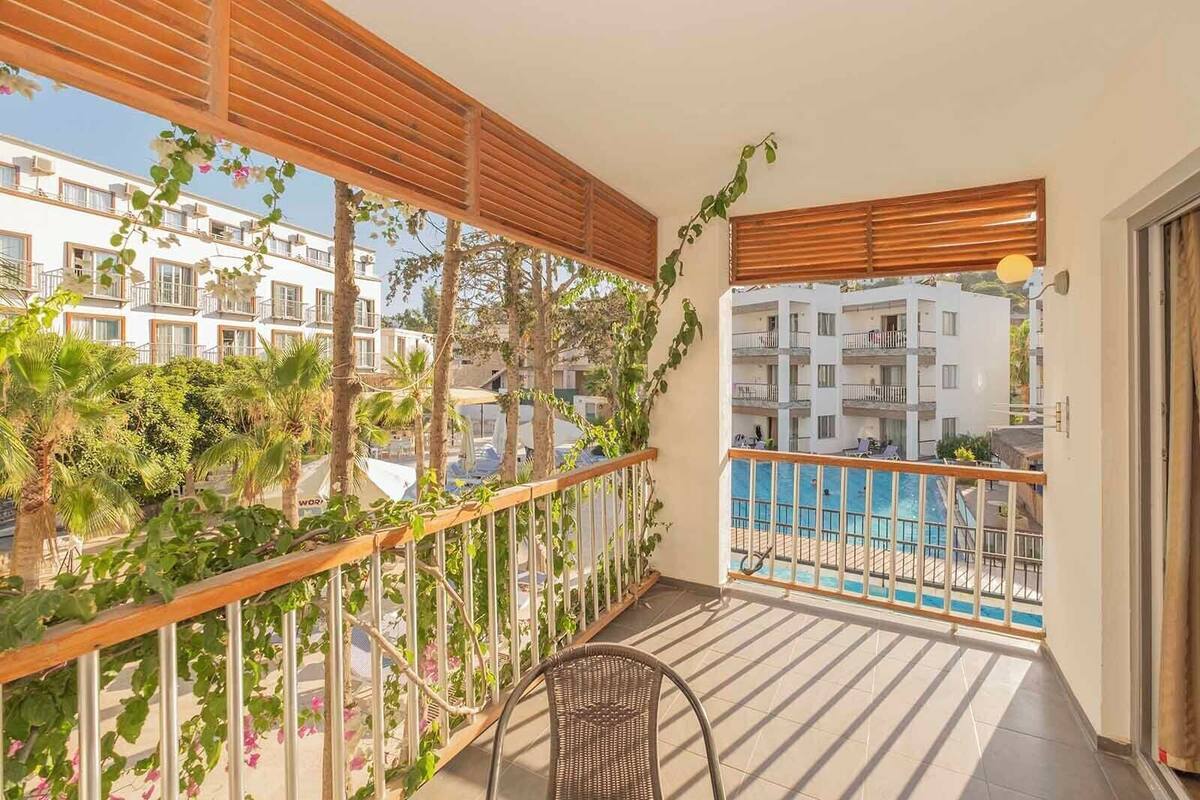 Un balcó amb vista a una piscina, envoltat de plantes i una barana de fusta.