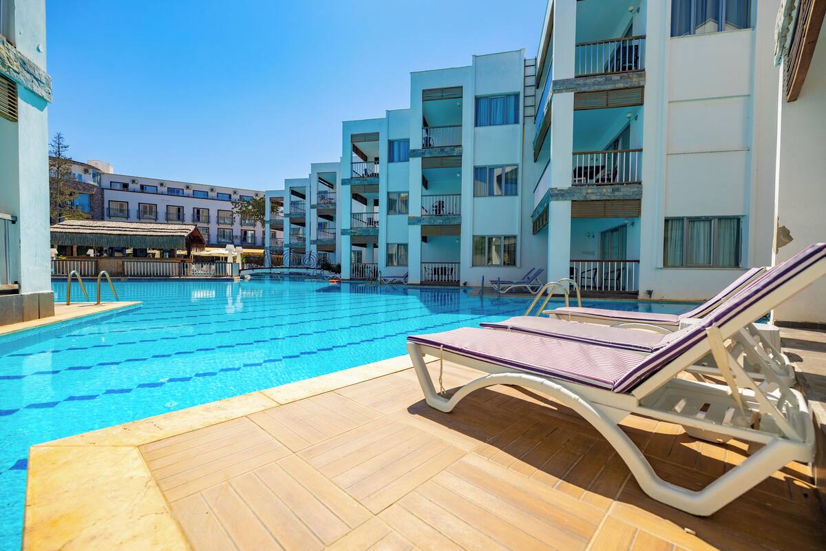 Zona de piscina amb gandules i un edifici amb balcons.