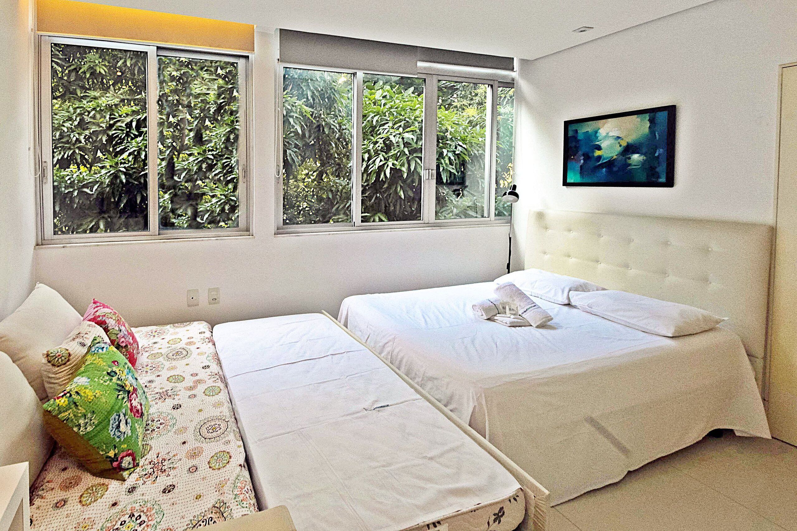 A bedroom with two beds, a window with a view of greenery, and a painting on the wall.