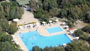 An aerial view of a resort with two swimming pools, surrounded by lush greenery and equipped with sun loungers and umbrellas.