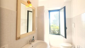 Een moderne badkamer met een wastafel, toilet en bad. Er is een raam met uitzicht op de omgeving.