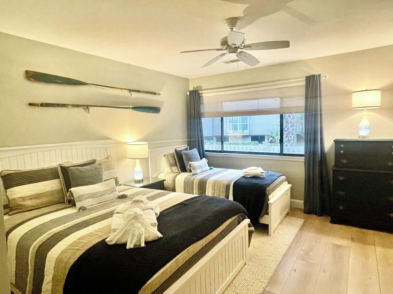 A hotel room with two beds, a ceiling fan, a window with curtains, and a dresser.