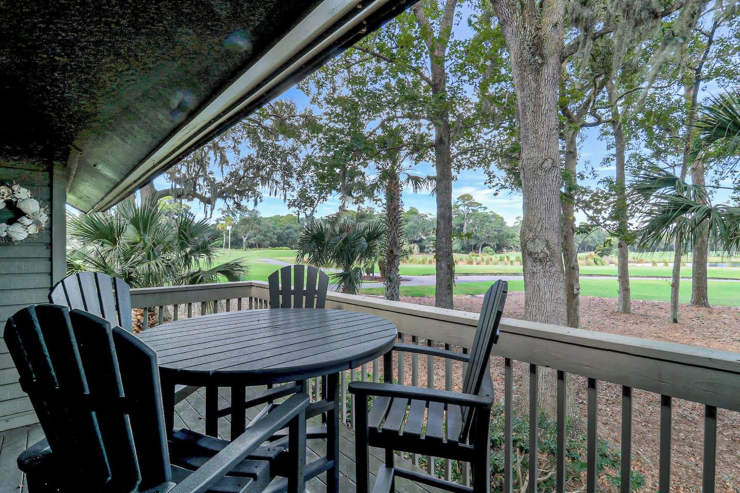Un área de estar al aire libre techada, con mesa y sillas, con vistas a un campo de golf.