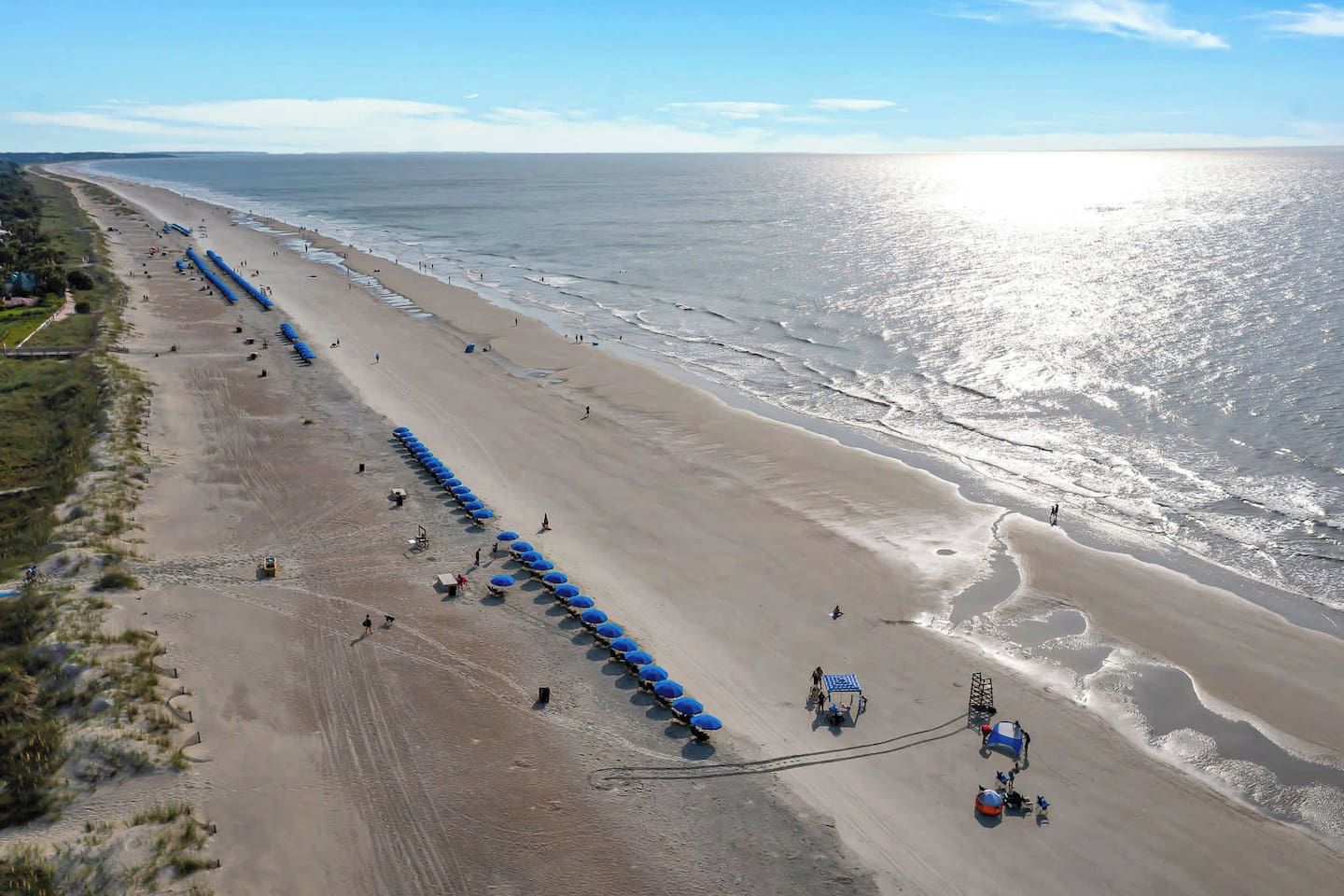 Une plage bordée d’une longue rangée de parasols bleus et de chaises de plage, un rivage sablonneux et l’océan.