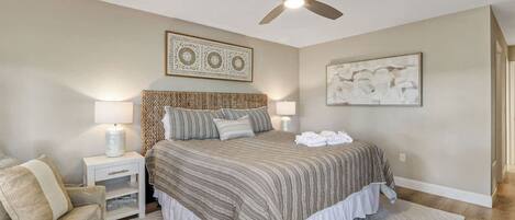 A bedroom with a bed, nightstands, a ceiling fan, and artwork on the walls.