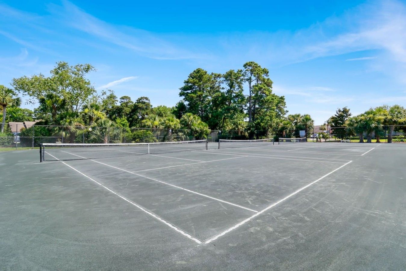 A tennis court with a net, surrounded by trees and a clear sky.