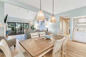 Uma sala ampla com uma mesa de jantar, cadeiras e um sofá. Há uma cozinha com armários e bancada.