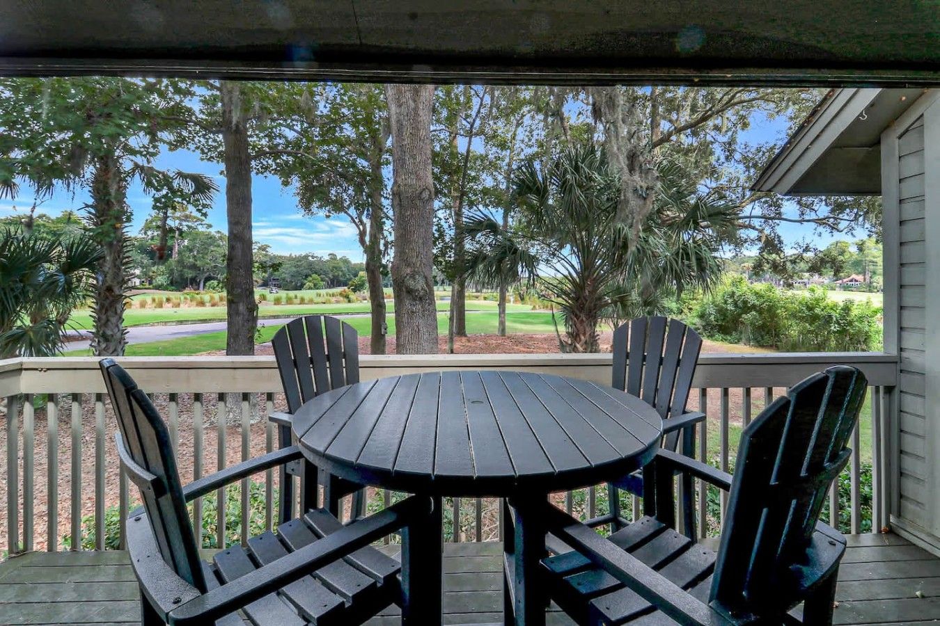 A covered outdoor seating area with a round table and four chairs, overlooking a golf course.
