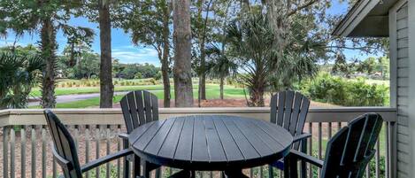 A covered outdoor seating area with a round table and four chairs, overlooking a golf course.
