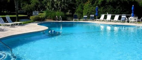 Une piscine d’un bleu éclatant, dotée de chaises longues et de parasols, et entourée de verdure.