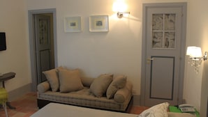 A room with a beige sofa, a bed, a door with a bird pattern, and two framed pictures on the wall.
