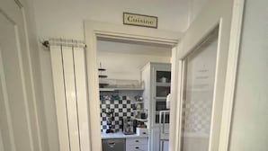 A narrow hallway leading to a kitchen with a checkered backsplash and white cabinets.