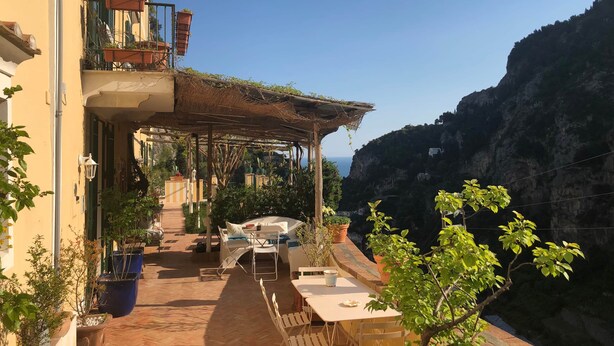 A terrace with outdoor seating, potted plants, and a view of a cliff.