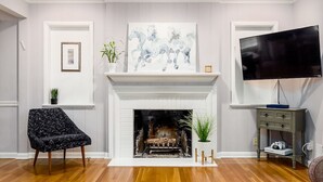 Un salon avec une cheminée, un téléviseur fixé au mur et un tableau au-dessus.