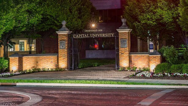 L’entrée de l’université Capital se distingue par sa façade en briques, son grand portail en arc de cercle et un jardin bien entretenu.