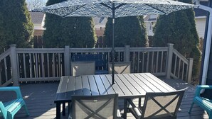 Une terrasse en bois avec une table et des chaises, un parasol et une rambarde.
