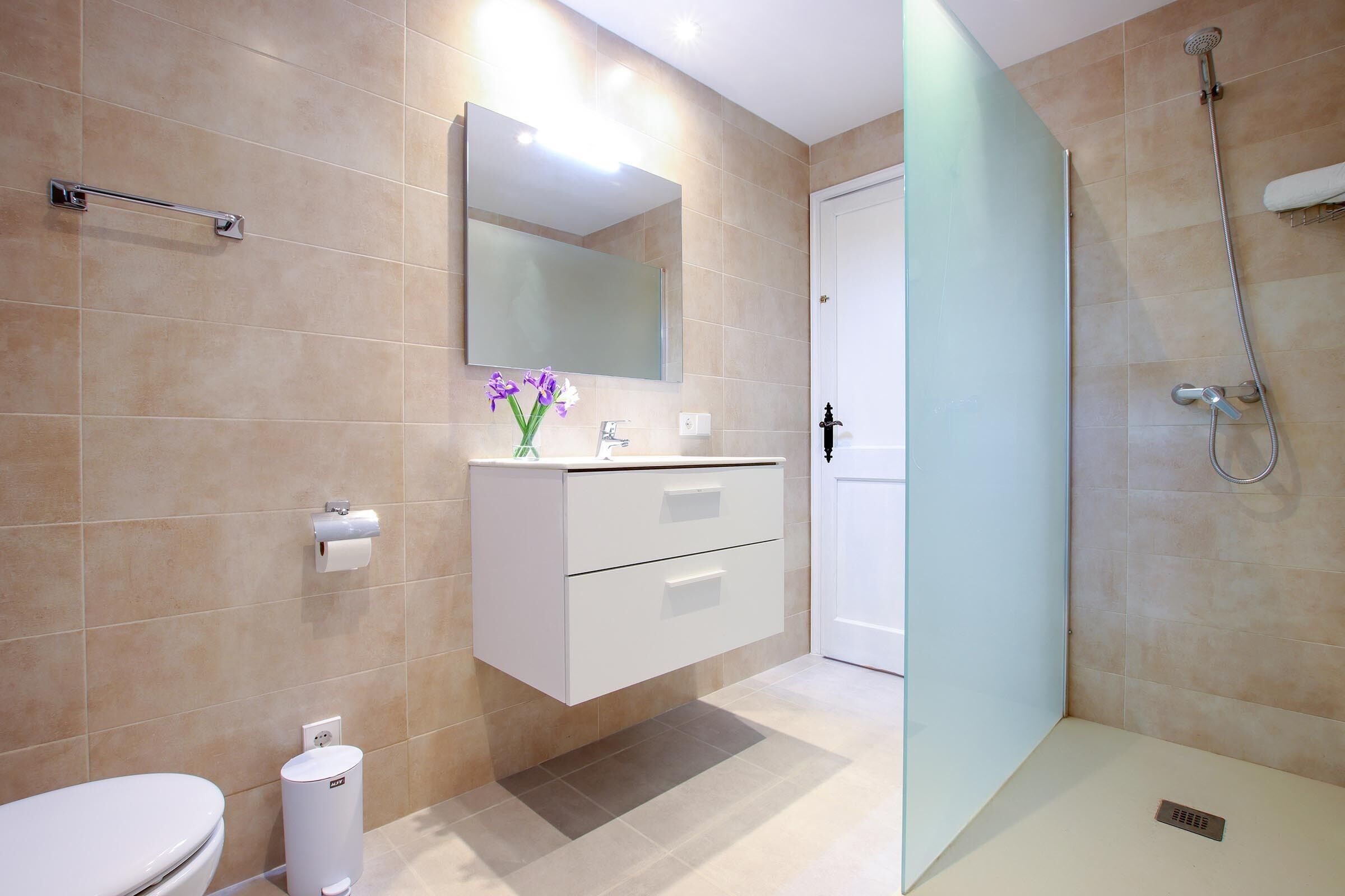 A modern bathroom with a toilet, sink, mirror, and shower.