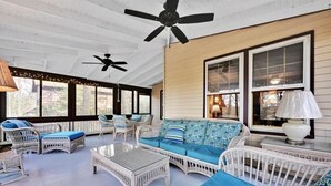 Une terrasse couverte, aménagée avec des meubles en osier, des ventilateurs de plafond et de grandes fenêtres.