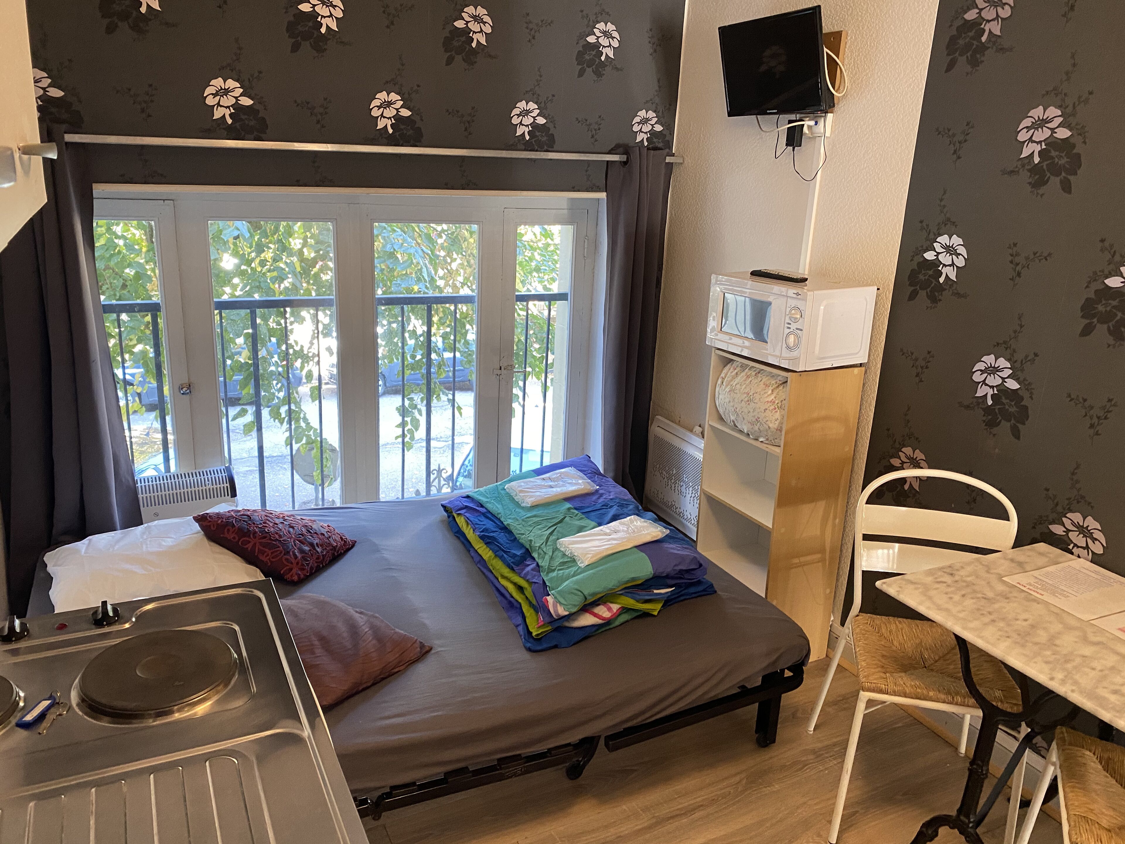 Una habitación compacta con cama, una kitchenette pequeña, una mesa de comedor y un televisor montado en la pared.