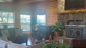 A cozy living room with a fireplace, a television mounted on the wall, and a ceiling fan. - The Lodge @ Stormy Mountain Ranch Close drive to Emience and surrounding springs (Birch Tree)