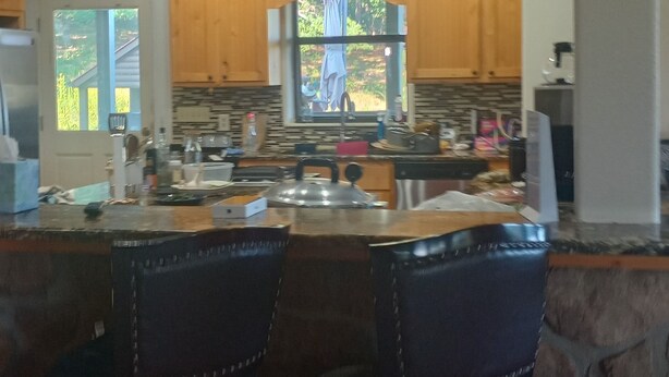 A kitchen with wooden cabinets, a large island with bar stools, and a view through a window. - The Lodge @ Stormy Mountain Ranch Close drive to Emience and surrounding springs (Birch Tree)