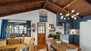 Una sala de estar acogedora con techo de madera, una mesa de comedor y una zona de cocina con armarios azules.
