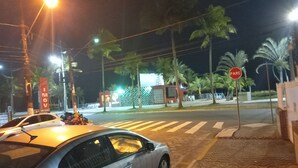 Une scène de rue nocturne avec une voiture garée sur le bord, des palmiers et un panneau de signalisation indiquant un arrêt obligatoire.