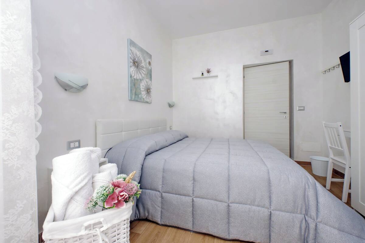A bedroom with a bed, a white chair, a wall-mounted shelf, and a door.