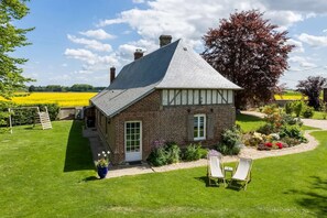 A traditional stone house with a gabled roof, a small porch, and a garden with flowers and a swing set.