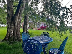 A garden with a table and chairs, a large tree, and a building in the background.
