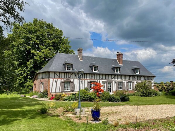 A traditional half-timbered house with a sloped roof, multiple chimneys, and a well-maintained garden with a lawn and flower beds.