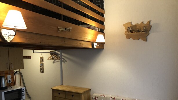 A cozy living room with a sofa, wooden dresser, and a wall-mounted shelf.