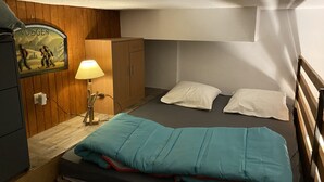 A compact room with a single bed, a wooden wardrobe, a lamp, and a wall-mounted picture.