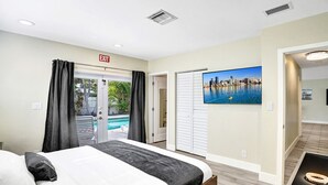 A hotel room with a bed, an exit sign, a view of a cityscape, and a pool outside.