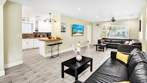 A modern living room with a black leather sofa, a coffee table, and a kitchen area with white cabinets and a wooden countertop.