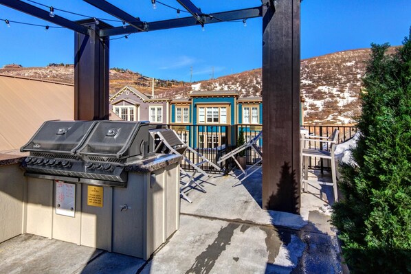 A barbecue grill with a sign, a staircase leading to a building, and a view of a residential area with houses and a hill in the background.