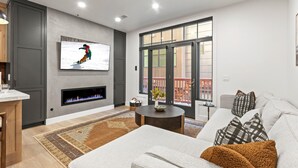 Una sala de estar moderna con chimenea, un televisor grande y vistas al exterior a través de un ventanal corredero.