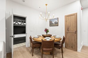 A dining area with a round table, wooden chairs, a chandelier, and a painting on the wall.