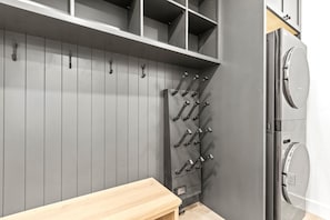 A laundry room with a washing machine, a drying rack, and a wooden bench.