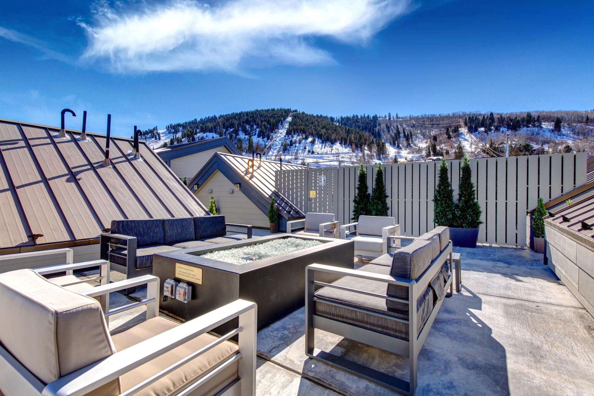 Une terrasse sur le toit avec des sièges extérieurs, un jacuzzi et une vue sur un paysage montagneux enneigé.