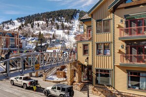 A multi-story building with balconies, a pedestrian bridge, and a snowy mountain backdrop. - Lift Lodge 103 Walk to Ski Lift, Elevator Access, On Main St, Common Hot Tub, Parking, Views! LLC-103 by KBM (Park City)