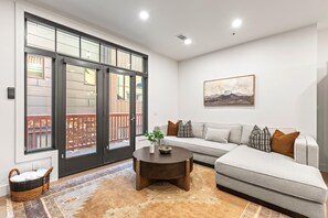 A living room with a gray sofa, a coffee table, and a large window with a view of a wooden deck.